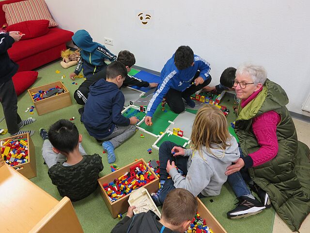 Viele Kinder bauen auf dem Bauteppich eine Stadt aus Lego