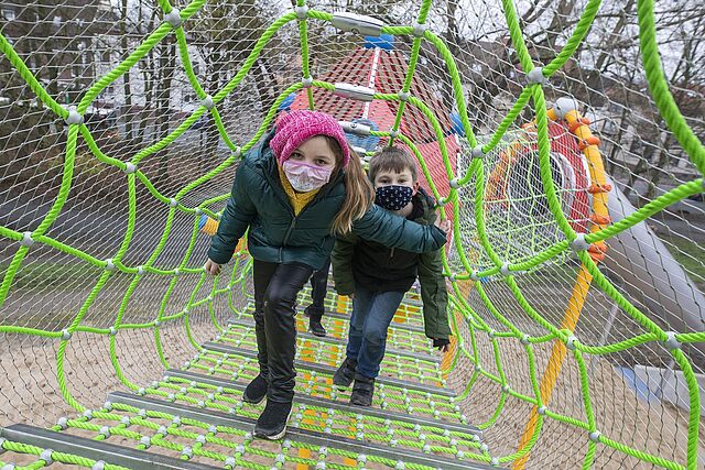 Ein Mädchen mit pinker Mütze und ein Junge klettern auf dem Spielplatz
