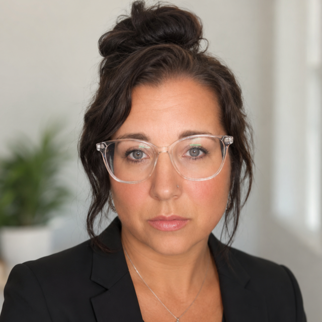 Eine junge Frau mit hochgesteckten Haaren und Brille schaut in die Kamera.