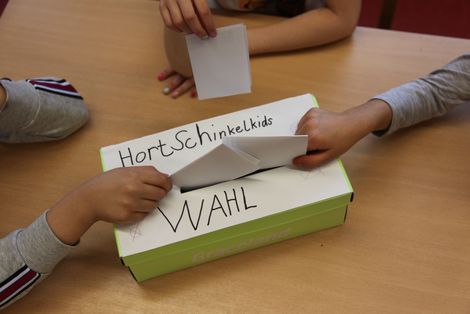 drei Kinder werfen ihre Stimmzettel in eine Box ein