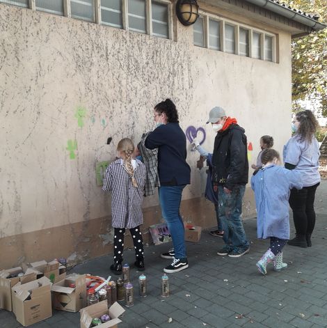 Kinder und Erwachsene verschönern die Turnhallenwand mit Graffiti