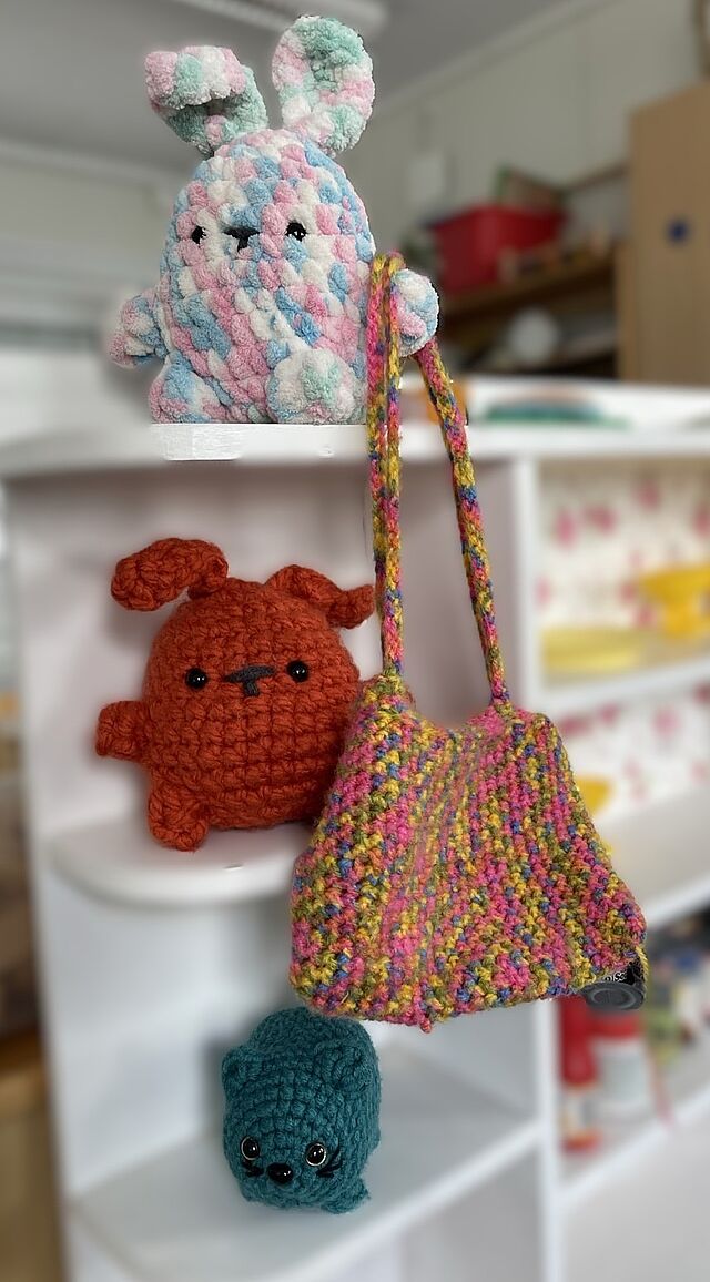 Es sind drei kleine gehäkelte Plüschtiere zu erkennen, sowie eine kleine gehäkelte Tasche.