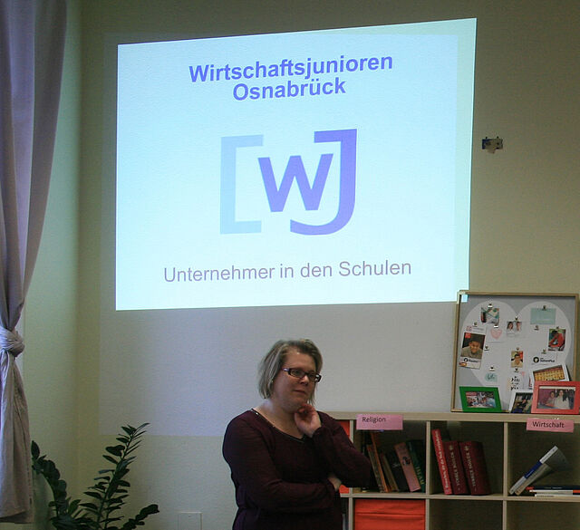 Eine junge Frau steht vor dem Loge der Wirtschaftsjunioren und hört aufmerksam zu.
