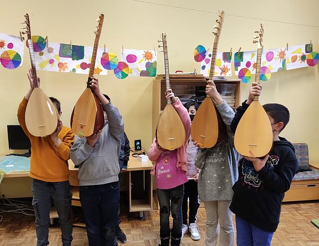 Fünf Kinder halten jeweils eine Saz, türkische Gitarre, hoch.