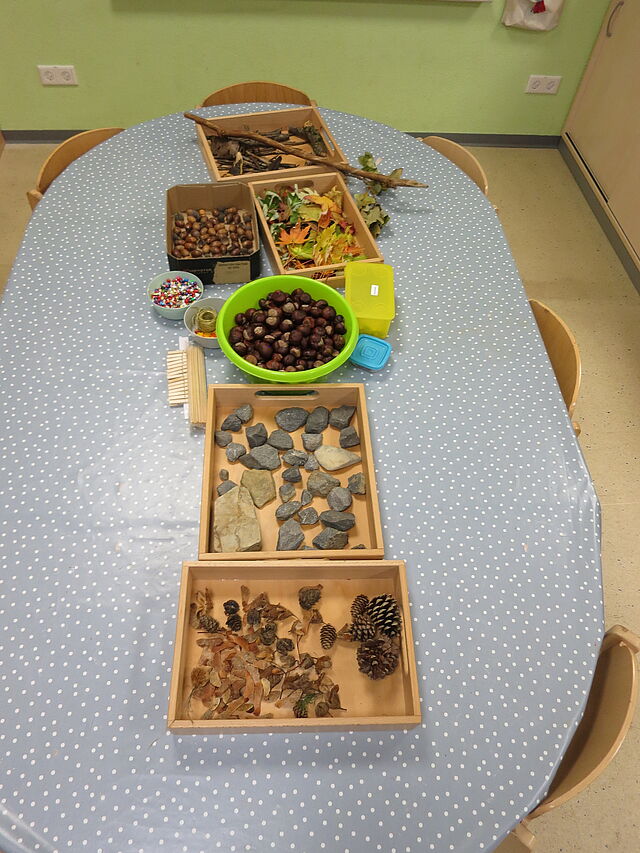 Verschiedene Naturmaterialien, wie Kastanien, Eicheln und kleine Steine liegen auf einem Tisch bereit.