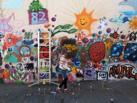 Ein Mädchen mit Graffitidose schaut auf die besprüte Wand