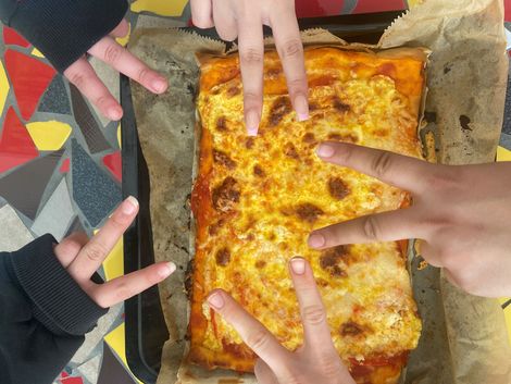 Fünf Hände machen das Victory-Zeichen über einer Pizza.