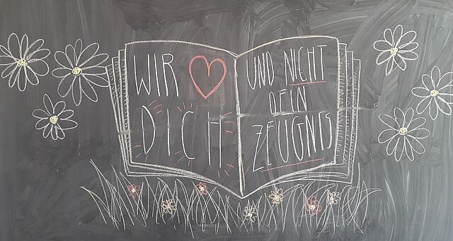 An der Tafel sind mit bunter Kreide Blumen und ein Heft gemalt. Es steht in dem Haft: Wir lieben dich und nciht dein Zeugnis.