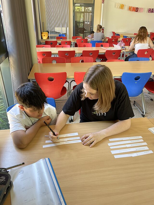 eine Studentin übt mit einem Kind eine Deutschaufgabe