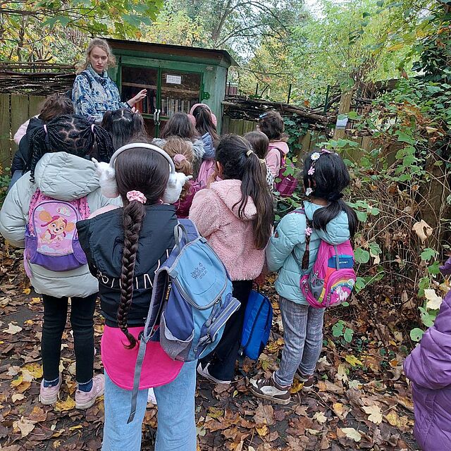 Eine Mitarbeiterin aus dem Hort zeigt den Kindern den Bücherschrank im Bürgerpark.
