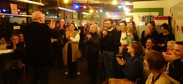 Die Gäste des Neujahrsempfangs singen ein Lied und klatschen im Takt. 
