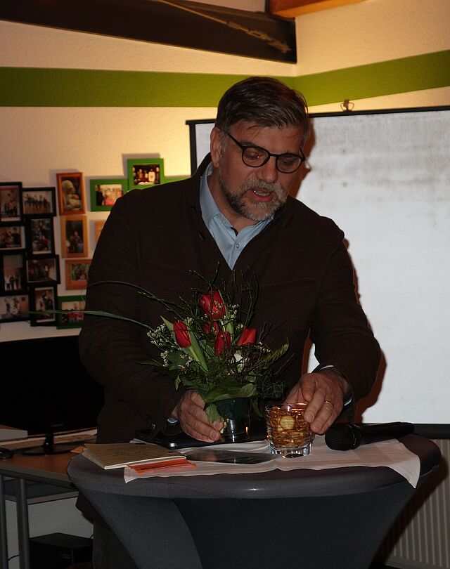 Mann mit Bart hält einen Vortrag an einem Tisch mit Blumen.