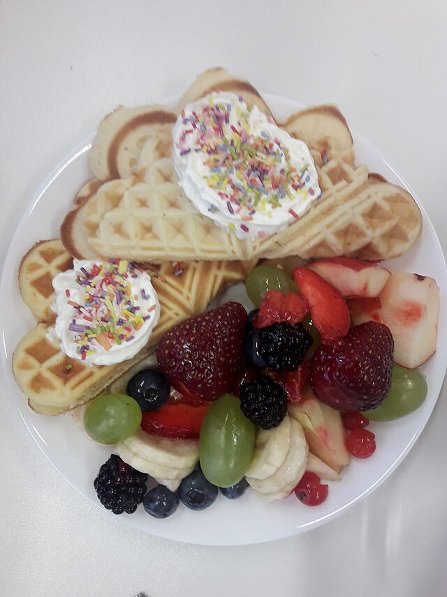 Auf einem Teller sind Waffeln, Sahne mit Streusel und Obst.