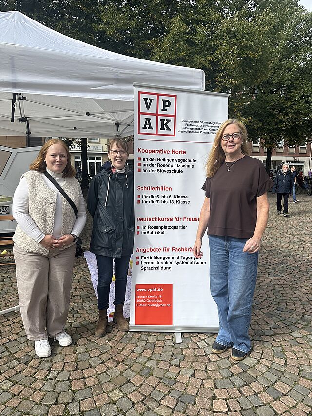 Drei Frauen lächeln vor einem Aufsteller in die Kamera.