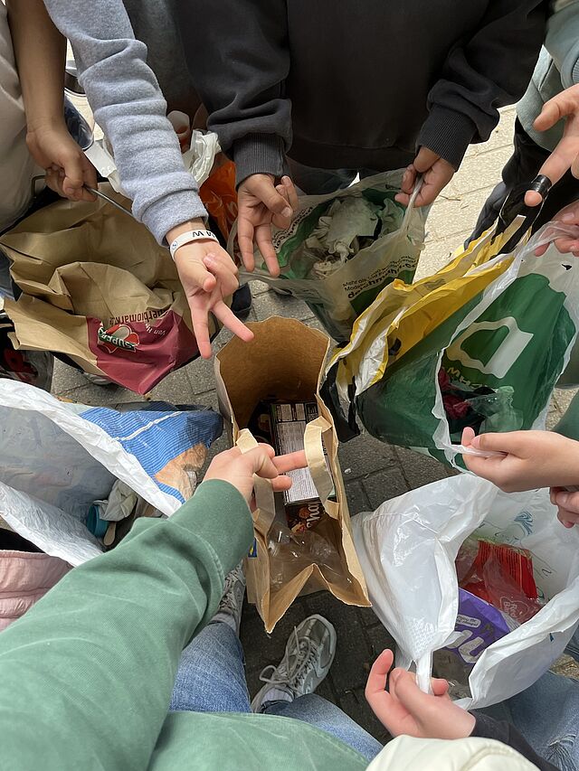 Es sind mehrere Hände zu sehen, die volle Mülltüten in die Kamera halten.