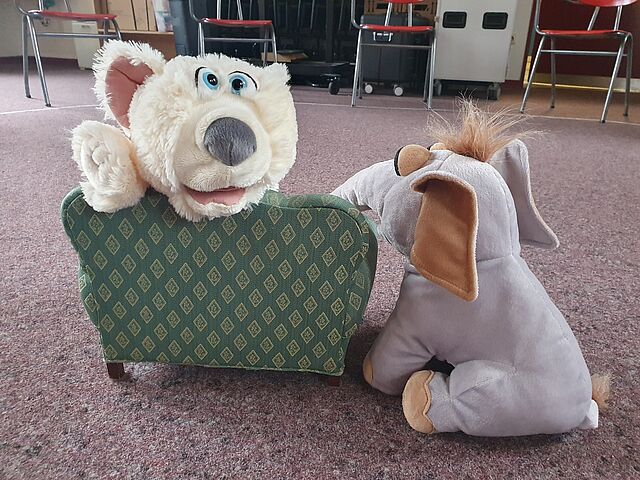 ein Plüschbär sitzt auf einem Puppensofa, ein Plüschelefant sitzt auf dem Boden