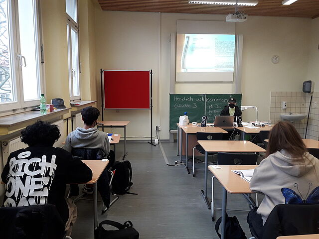 In einem Klassenraum lernen Jugendliche an Schultischen sitzend.