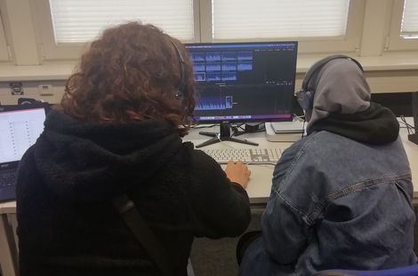 Zwei Jugendliche bearbeiten ihren Podcast am PC.