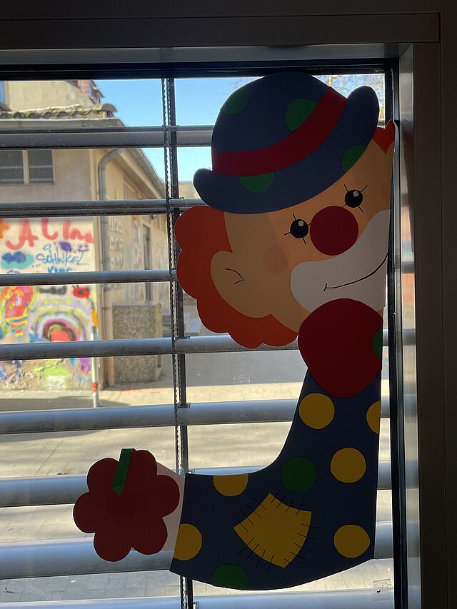 Ein bunter aus Tonkarton gebastelter Clown klebt am Fenster.
